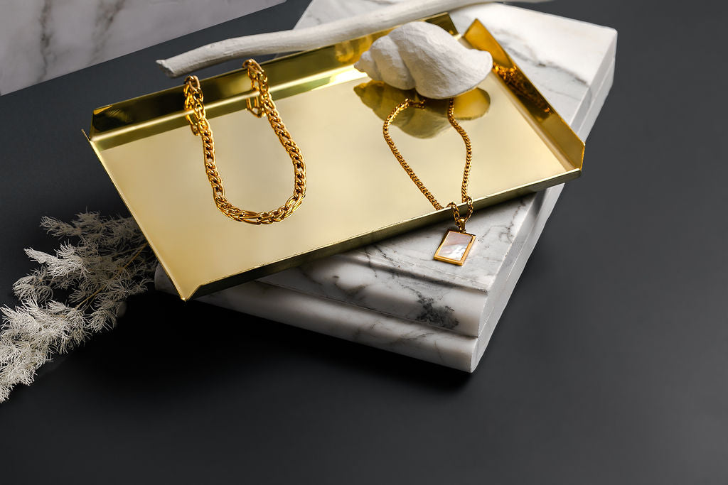 A polished brass tray, shaped as a rectangle sitting atop a marble slab.