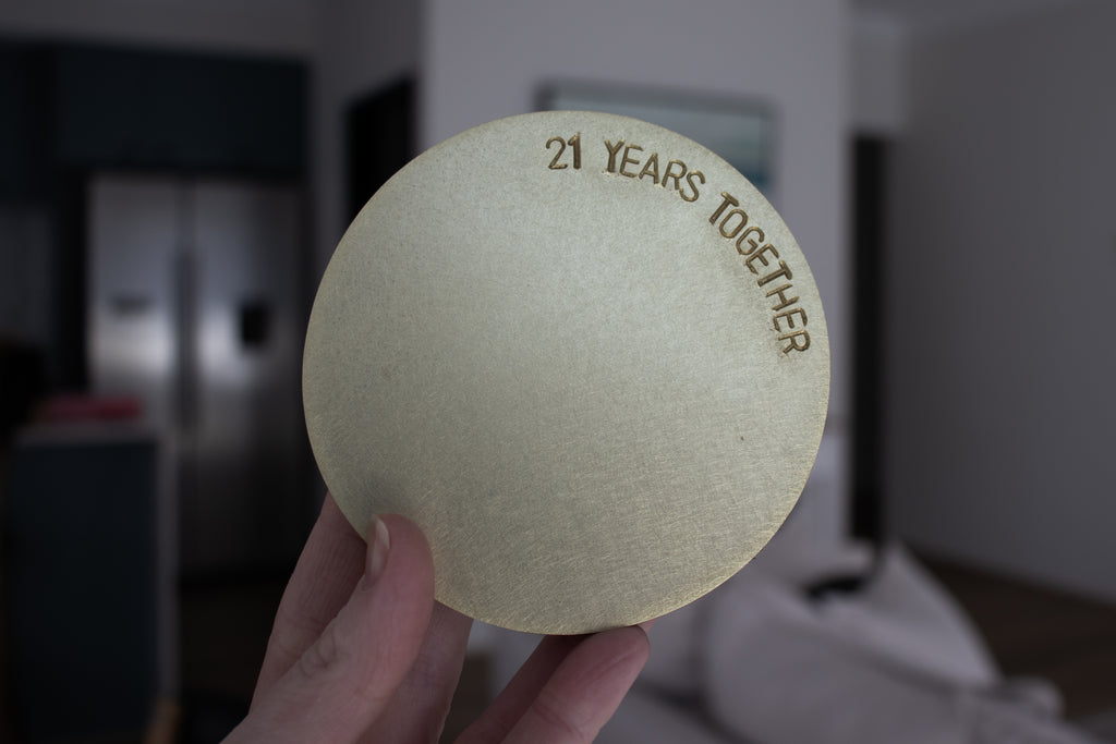 A close up picture of one, brushed brass coaster engraving with the words 21 Years Together. The coasters are made by Empire Copper.